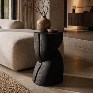 Könnte beinhalten: Ein schwarzer Beistelltisch aus Holz mit einem einzigartigen, geschnitzten Design. Eine kleine, runde, beige Vase hält getrocknete Zweige. Eine kleine, runde, beige Schale steht auf dem Tisch. Der Tisch steht in einem Raum mit neutralen Tönen.