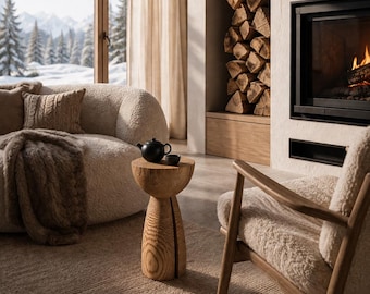 Op de afbeelding: Een gezellige woonkamer met een open haard, een comfortabele bank en een houten bijzettafel. Een zwarte theepot en kopje staan op de tafel. De kamer heeft een neutraal kleurenpalet met uitzicht op een besneeuwd berglandschap.