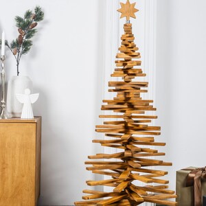 May include: A tall, conical Christmas tree sculpture constructed from stacked, horizontal wooden slats in a medium brown finish. The structure features a central vertical support and is topped with a carved wooden star ornament.