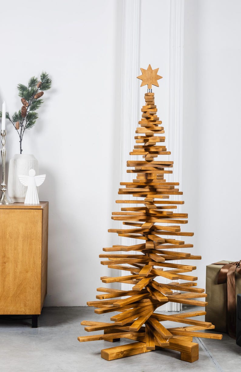 May include: A tall, conical Christmas tree sculpture constructed from stacked, horizontal wooden slats in a medium brown finish. The structure features a central vertical support and is topped with a carved wooden star ornament.