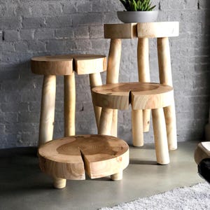 Op de afbeelding: Vier houten krukken in verschillende maten, elk met een ronde bovenkant en vier poten. De krukken zijn gemaakt van natuurlijk hout en hebben een rustieke, handgemaakte uitstraling.