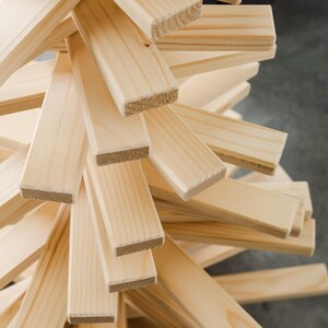 May include: A decorative tree sculpture constructed from numerous light-colored, unfinished wooden slats arranged in a spiraling, layered pattern. The rectangular pieces of wood feature visible grain and texture, radiating outward from a central vertical axis.