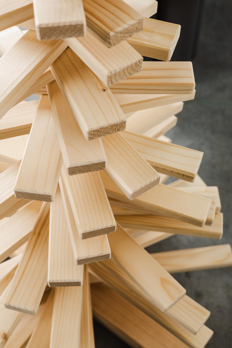 May include: A decorative tree sculpture constructed from numerous light-colored, unfinished wooden slats arranged in a spiraling, layered pattern. The rectangular pieces of wood feature visible grain and texture, radiating outward from a central vertical axis.