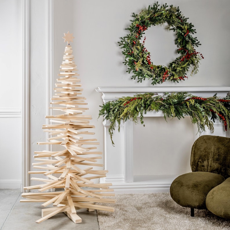 May include: A tall, conical Christmas tree sculpture constructed from stacked, horizontal light-colored wooden slats. The structure features a central vertical support and a small, star-shaped wooden topper, creating a layered, geometric silhouette.