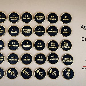 Może przedstawiać: Zestaw 24 czarnych i złotych okrągłych żetonów z różnymi symbolami i tekstami, w tym "+1 do ranienia", "Uderzenie ostatnie", "6+ Osłona", "Atak totalny" i "Biegnij i atakuj". Żetony są ułożone w siatkę na brązowej powierzchni. Tekst "Age of Sigmar Essentials V2" i logo "TAB Tabletop and Beyond" są widoczne w górnej części obrazu.