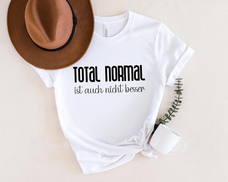 May include: White t-shirt with black text that reads "Total Normal ist auch nicht besser".