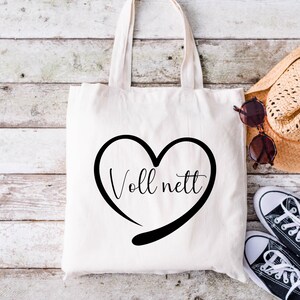 May include: A white tote bag with black handles and a black heart design that says "Voll nett" in a cursive font.