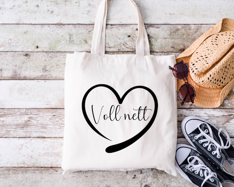 May include: A white tote bag with black handles and a black heart design that says "Voll nett" in a cursive font.