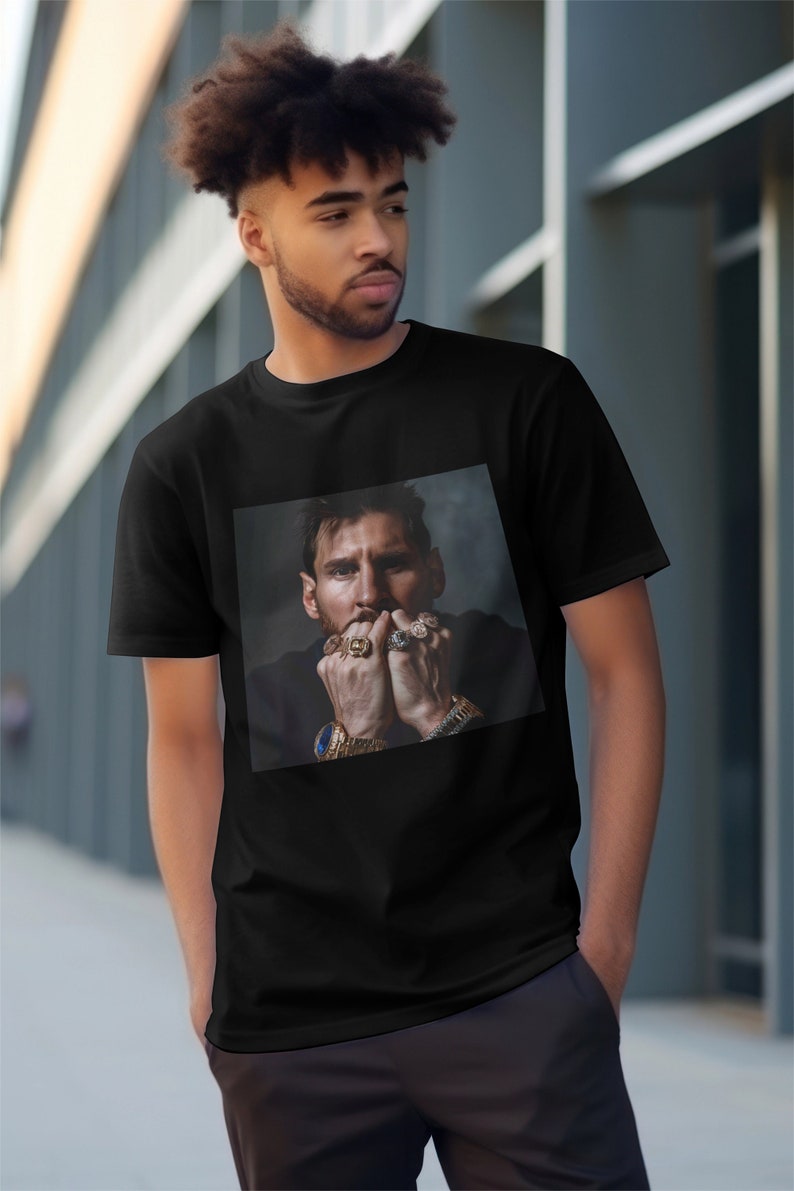 May include: A black t-shirt featuring a printed image of a man with a beard wearing a gold watch and several rings on his fingers.