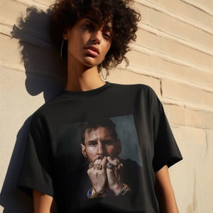 May include: A black t-shirt featuring a graphic print of a man wearing several rings and a watch. The man has a beard and short brown hair.