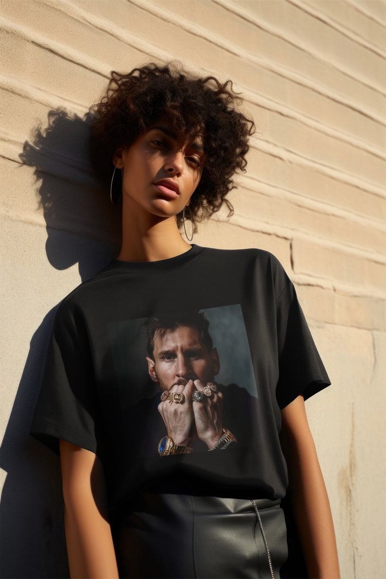 May include: A black t-shirt featuring a graphic print of a man wearing several rings and a watch. The man has a beard and short brown hair.