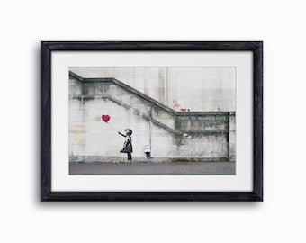 Puede incluir: Un stencil en blanco y negro de una niña soltando un globo rojo en forma de corazón en una pared de concreto gris con las palabras "There is always hope" escritas en ella.