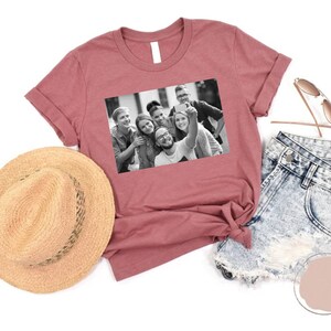 May include: A maroon t-shirt with a black and white photo of a group of friends taking a selfie. The photo shows six people smiling and looking at the camera.
