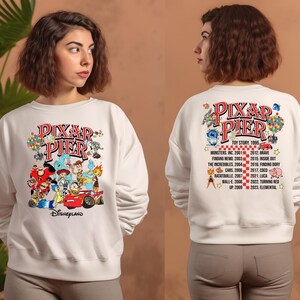 May include: White sweatshirt with a colorful graphic of Pixar characters and the text "Pixar Pier" and "Disneyland". The back of the sweatshirt has a list of Pixar movies and their release years.