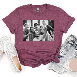 May include: A maroon t-shirt with a black and white photo of a group of friends taking a selfie. The photo shows six people smiling and looking at the camera.