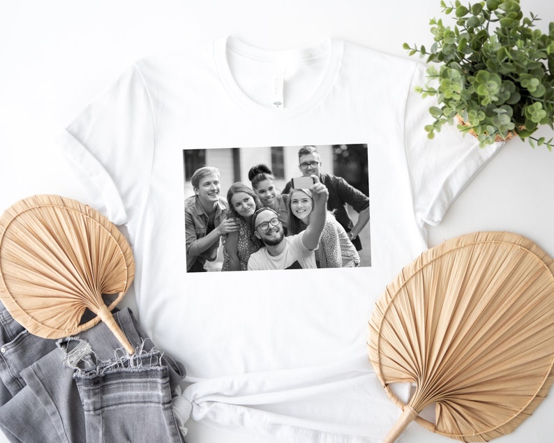 May include: Black and white photo of a group of friends taking a selfie. The friends are smiling and appear to be having fun. The photo is printed on a white t-shirt.