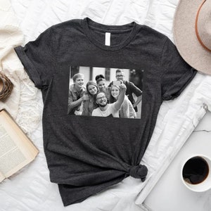 May include: A dark gray t-shirt with a black and white photo of a group of friends taking a selfie. The photo shows six people smiling and looking at the camera.