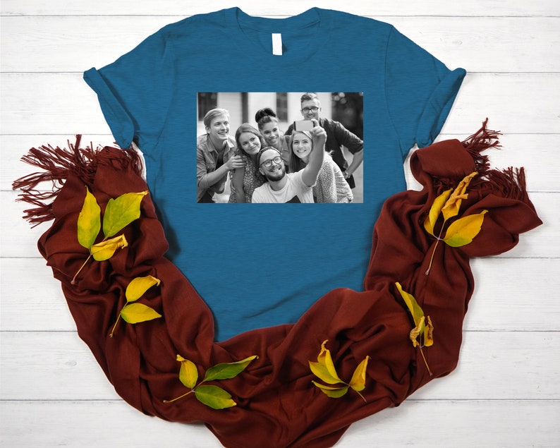 May include: A teal blue t-shirt with a black and white photo of a group of friends taking a selfie. The photo shows six people smiling and looking at the camera.