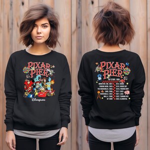 May include: Black sweatshirt with a colorful graphic of Pixar characters and the text "Pixar Pier" and "Disneyland". The back of the sweatshirt features a list of Pixar movies and their release years.
