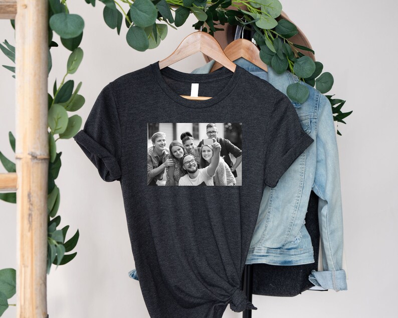 May include: A dark heather grey t-shirt with a black and white photo of a group of friends taking a selfie. The photo shows six people smiling and looking at the camera.