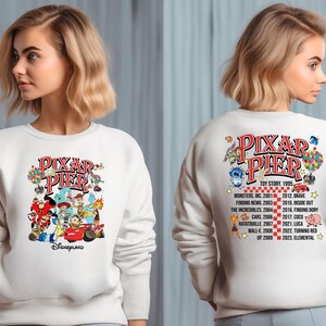 May include: White sweatshirt with a colorful graphic of Pixar characters and the text "Pixar Pier" on the front. The back of the sweatshirt has a list of Pixar movies and their release dates.