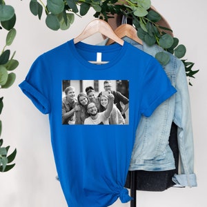 May include: A royal blue t-shirt with a black and white photo of a group of friends taking a selfie.