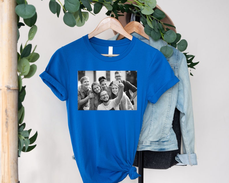 May include: A royal blue t-shirt with a black and white photo of a group of friends taking a selfie.