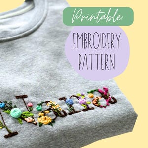 May include: Printable embroidery pattern for the word "Mommy" with floral accents. The pattern is displayed on a gray sweatshirt.