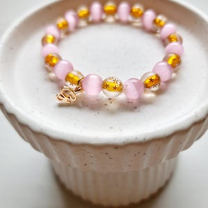 May include: A pink and gold beaded bracelet with a gold charm that says "2023".