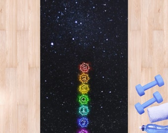 Puede incluir: Una esterilla de yoga negra con un diseño de noche estrellada y una fila vertical de siete chakras coloridos en el centro.