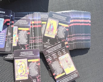 May include: A deck of tarot cards with a black and gold design, featuring illustrations and text. The cards are spread out, with some stacked and others fanned. A box with the words "Tarot for Beginners" is visible.