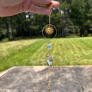 May include: Gold sun and crystal suncatcher with a small gold feather charm hanging from a black cord.