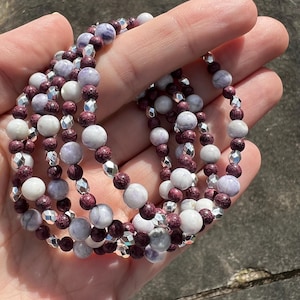 May include: A multi-strand bracelet with purple, white, and silver beads. The beads are round and have a smooth, polished finish.