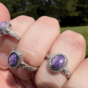 May include: Two silver rings with oval-shaped purple stones set in a decorative bezel. The rings have a detailed, ornate design.