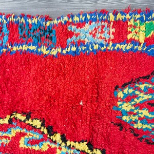 May include: A red, blue, yellow, and green Moroccan rug with a geometric pattern. The rug has a fringe border.