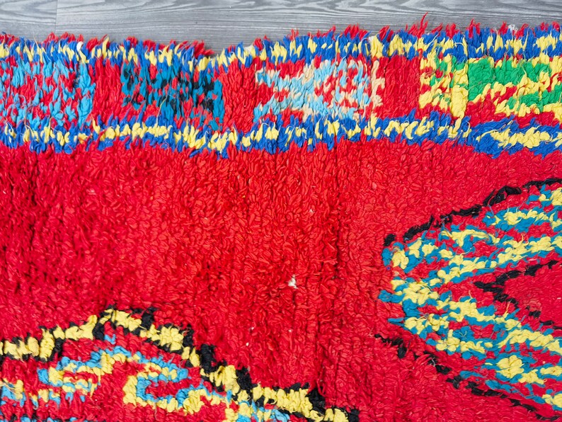 May include: A red, blue, yellow, and green Moroccan rug with a geometric pattern. The rug has a fringe border.