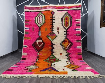 May include: A vibrant, hand-woven rug with a bold geometric design. The rug features a striking color palette of hot pink, orange, and white, with accents of green, blue, and brown. The central design includes diamond and geometric shapes.