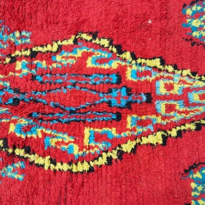 May include: A red rug with a geometric pattern in blue, yellow, and black. The pattern is made up of squares and diamonds.