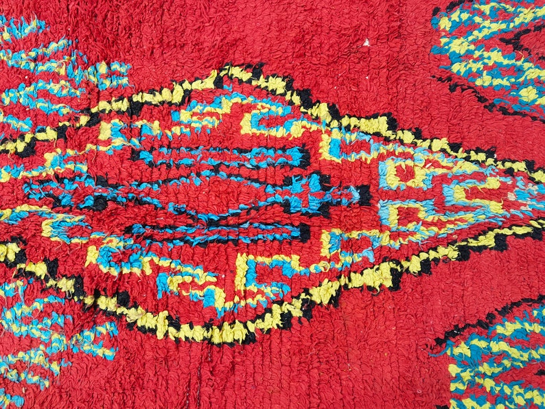 May include: A red rug with a geometric pattern in blue, yellow, and black. The pattern is made up of squares and diamonds.