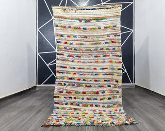 May include: A white, handwoven rug with colorful stripes and a fringe border. The rug is made of recycled materials and has a unique, bohemian style.