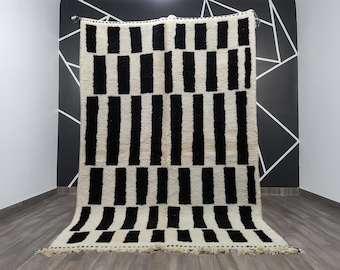 May include: A large, rectangular rug with a cream-colored background and bold black vertical stripes. The rug has a textured appearance and a fringed edge. The design is geometric and modern, suitable for a living room or bedroom.