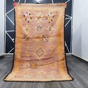 Puede incluir: Una alfombra marroquí vintage con fondo rosa y intrincados patrones geométricos en tonos naranja, amarillo y azul.