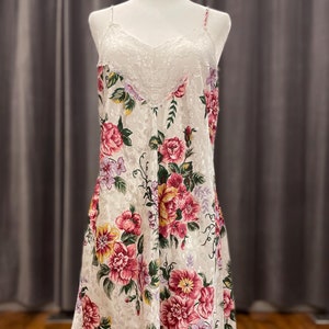 May include: A white slip dress with a floral print and lace trim. The dress has a scoop neck and thin straps.