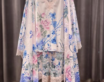以下が含まれることがあります： 白、ピンク、青の3ピースフローラルパジャマセット。セットには、レーストリム付きのキャミソール、お揃いのショートパンツ、ロングローブが含まれています。ローブとショートパンツにはレーストリムが付いています。花柄にはバラやその他の花が描かれています。
