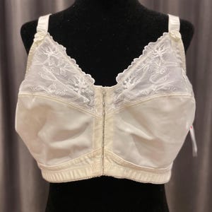 Op de afbeelding: Ivoor kleurige beha met een sluiting aan de voorkant en verstelbare bandjes. De bovenste cups hebben delicate kanten details met bloemmotieven. De beha wordt getoond op een zwarte mannequin, die het ontwerp benadrukt.