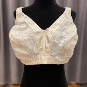 Op de afbeelding: Ivoor kleurige beha met een V-hals ontwerp. De beha heeft een bloemen kanten patroon op de cups en een satijnachtige afwerking op de bandjes en band. De beha wordt getoond op een zwarte mannequin.