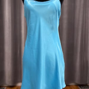 May include: A light blue slip dress with spaghetti straps. The dress is made of a silky material and has a simple, elegant design. The neckline and straps are trimmed with a delicate detail. The dress is displayed on a black mannequin.