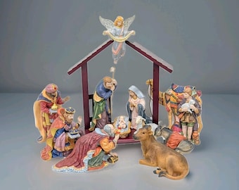 May include: A Christmas nativity scene with figurines of the Holy Family, the Three Wise Men, an angel, and animals. The figures are in various colors, with a wooden stable in the background.