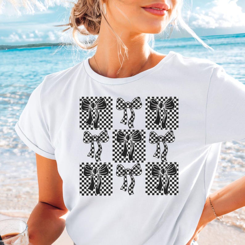 May include: White t-shirt with a black and white checkered pattern featuring black bows. The bows are arranged in a 3x3 grid.
