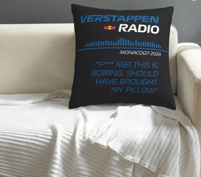 May include: Black square pillow with the text "VERSTAPPEN RADIO" in blue and white. Below the text is "MONACOGP 2024" and a quote that reads "F*** ME! THIS IS BORING, SHOULD HAVE BROUGHT MY PILLOW". The pillow is on a white couch.
